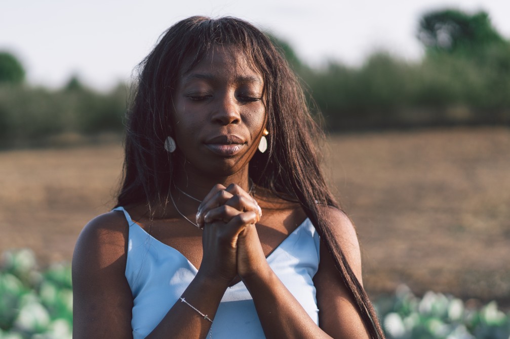 black woman with hands clasped and eyes closed standing in field - fighting racial injustice